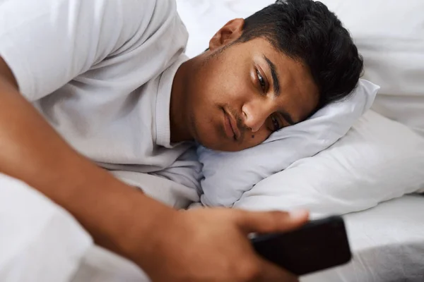 Still no text back from her. Shot of a young man using his cellphone while lying on his bed. — ストック写真