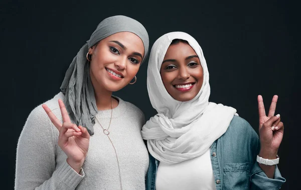 Tendências milenares. Tiro recortado de duas jovens mulheres atraentes vestindo hijabs e de pé juntos enquanto mostram um sinal de paz no estúdio. — Fotografia de Stock
