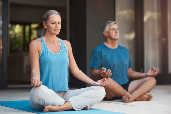 Fred kommer inom oss. Skott av ett moget par som lugnt engagerar sig i en yogapose med benen korsade. — Stockfoto