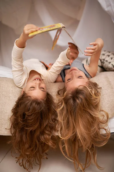 Girando la storia sulla sua testa. Girato di due bambine che leggono un libro sdraiate a testa in giù su un letto. — Foto Stock