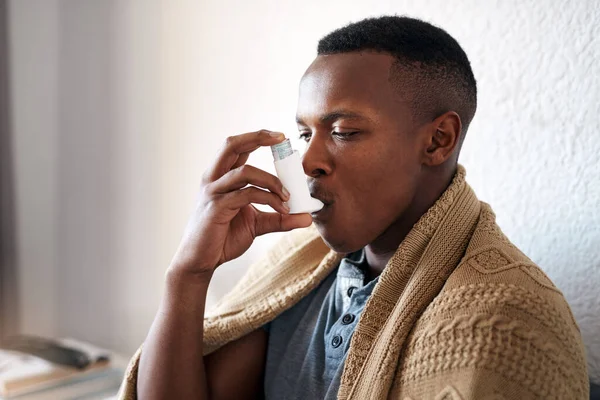 I really need my asthma pump. Cropped shot of a handsome young man sitting alone in his bedroom and using an asthma pump. — Stock Photo, Image