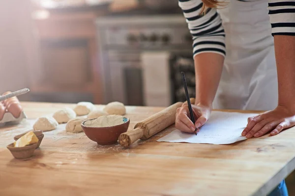 Uno aprende haciendo. Recorte de una mujer escribiendo una receta para la masa que ella está preparando. — Foto de Stock
