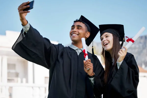 Adivinha o que todos nós fizemos. Tiro de dois jovens estudantes tirando selfies no dia da formatura. — Fotografia de Stock