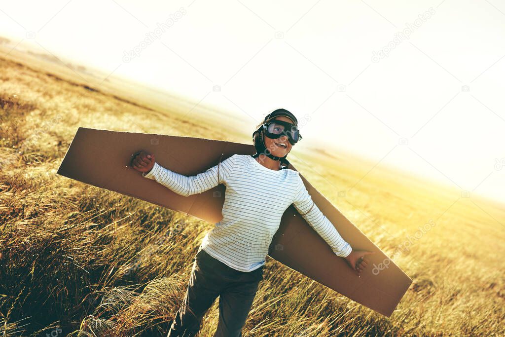 Childhood is a chance for magical adventures. Shot of a young boy pretending to fly with a pair of cardboard wings in an open field.