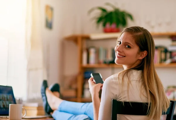 No puedo imaginar mi vida sin wifi. Retrato de una mujer joven usando su teléfono inteligente mientras está sentada en su escritorio en casa. —  Fotos de Stock