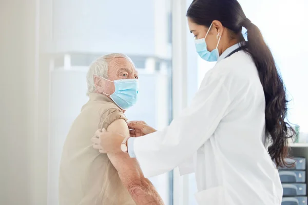 Itll be over before you know it. Shot of a doctor wearing a face mask and preparing her senior patient for a Covid vaccine in her clinic. —  Fotos de Stock