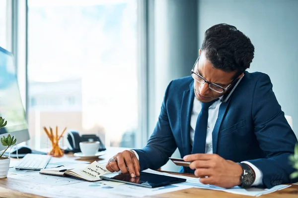 Hij neemt de beslissingen en neemt de belangrijke beslissingen. Opname van een gefocuste jonge zakenman zittend aan zijn bureau terwijl hij telefoneert en bladert op een digitale tablet in het kantoor. — Stockfoto