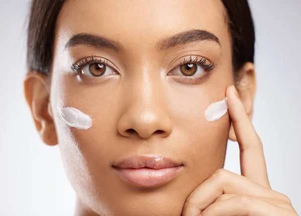 Its not magic, its moisturiser. Studio shot of an attractive young woman applying moisturiser to her face against a grey background. — Photo