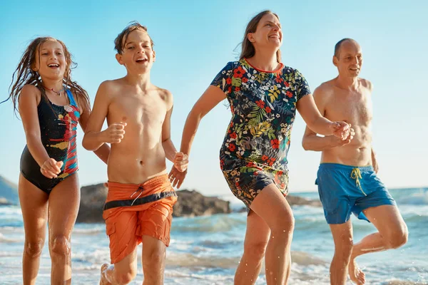 Vítěz dostane největší zmrzlinu. Zastřelen čtyřčlennou rodinou běžící společně na pláži. — Stock fotografie