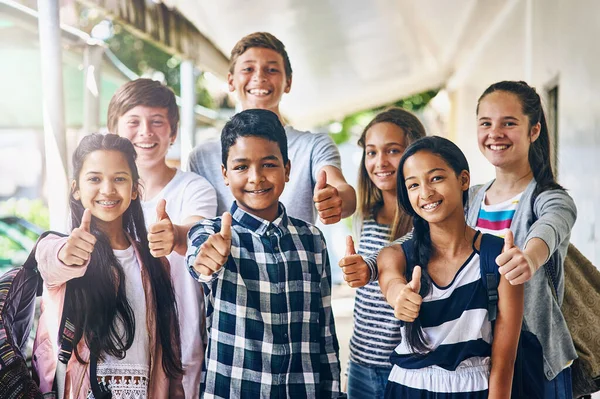 Vår skola är häftig. Porträtt av en grupp glada skolbarn som visar tummen upp utanför klassrummet. — Stockfoto