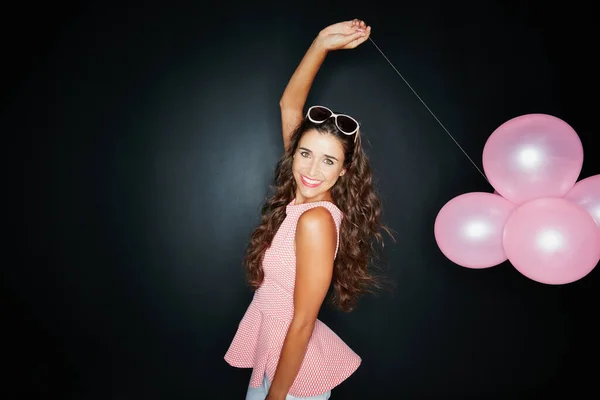 Sou a vida da festa. Retrato de estúdio de uma jovem atraente segurando balões contra um fundo escuro. — Fotografia de Stock