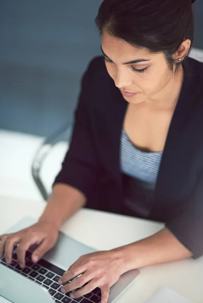 Skriver upp en storm. Hög vinkel skott av en attraktiv ung affärskvinna som arbetar på en bärbar dator på sitt kontor. — Stockfoto