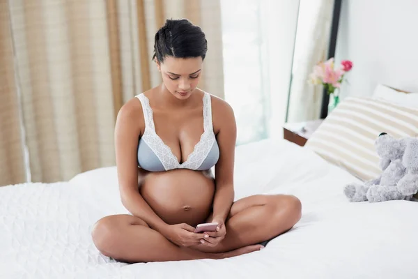 Herkes anne ve bebeğin nasıl olduğuyla ilgili güncelleme istiyor. Hamile bir genç kadının evinde yatağında cep telefonu kullanırken görüntüsü.. — Stok fotoğraf