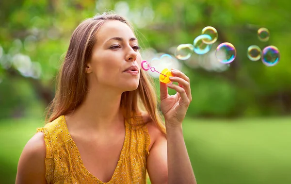 Tekrar küçük bir kız gibi hissediyorum. Parkta baloncuklar çıkaran kaygısız genç bir kadının fotoğrafı.. Telifsiz Stok Fotoğraflar