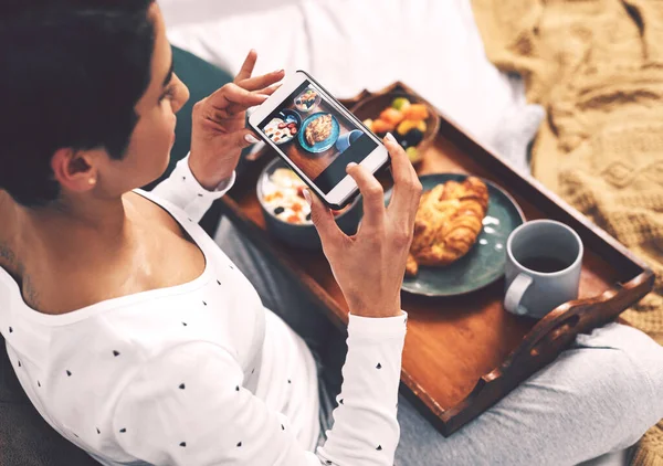 Machen Sie es für das Gramm. Schnappschuss einer attraktiven jungen Frau, die ihr Handy benutzt, um ihr Frühstückstablett zu Hause zu fotografieren. — Stockfoto