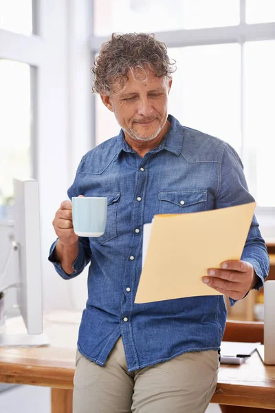 O café aguça-lhe a mente. Tiro de um homem de negócios maduro tomando café enquanto olha através de papelada. — Fotografia de Stock