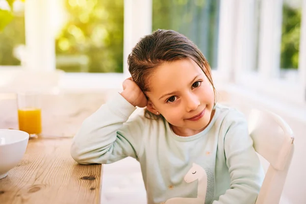 Je veux sortir jouer dehors. Portrait d'une petite fille joyeuse assise à côté d'une table de cuisine avec une main à côté de sa tête tout en regardant la caméra. — Photo