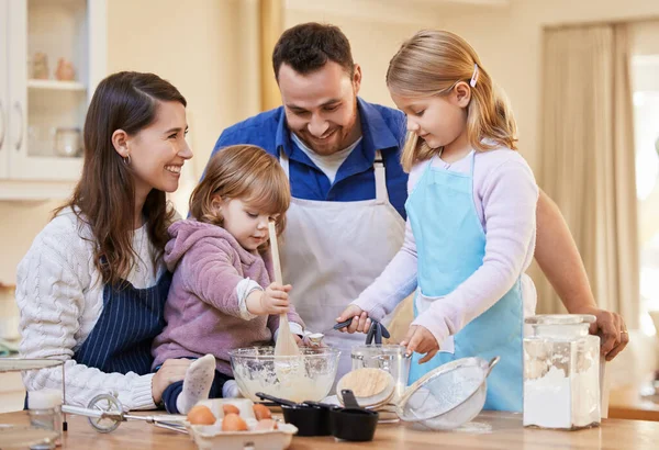 Familjetid är det enda viktiga. Skjuten av en familj bakar tillsammans medan en liten flicka rör en skål tårta smet. — Stockfoto