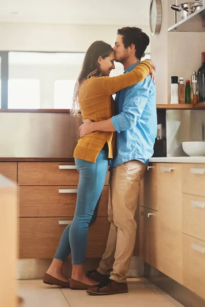 Förseglad med en kyss. Skjuten av en kärleksfull ung man kysser sin flickvän i pannan i deras kök. — Stockfoto