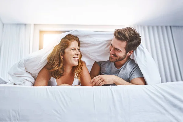 They fall more and more in love each day. Shot of a couple relaxing together underneath a blanket at home. — Stock Photo, Image