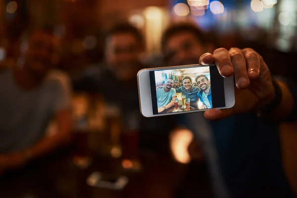 Isto está a acontecer, rapazes. Close-up de um grupo de jovens amigos alegres fazendo um auto-retrato juntos enquanto desfrutam de cerveja juntos em um bar durante a noite. — Fotografia de Stock