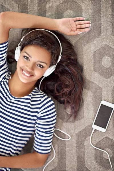 Mi godo la mia compagnia. Ritratto ad angolo alto di una giovane donna che ascolta musica sul suo cellulare mentre è sdraiata sul pavimento. — Foto Stock