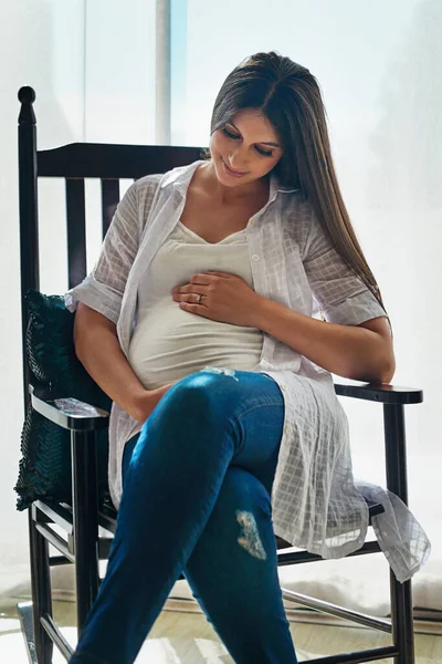 Contando i giorni che mancano al tuo arrivo. Girato di una donna incinta felice culla la pancia mentre si rilassa in una sedia a casa. — Foto Stock