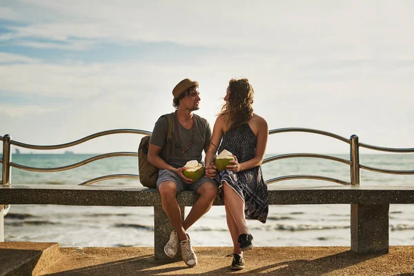 Rozmawiamy nad morzem. Strzał szczęśliwej młodej pary delektującej się koktajlami podczas relaksu na ławce przy plaży. — Zdjęcie stockowe