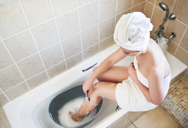 Pomyśl zanim się ogolisz, pomyśl o wodzie i oszczędzaj. Duże ujęcie młodej kobiety golącej nogi w wiadrze wody w łazience w domu. — Zdjęcie stockowe