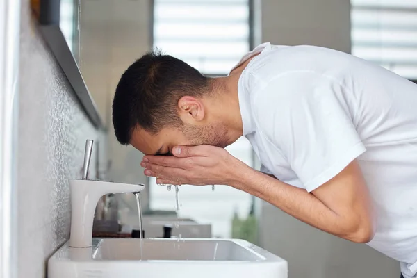 L'eau est idéale pour votre peau. Tourné d'un jeune homme se lavant le visage dans une salle de bain à la maison. — Photo