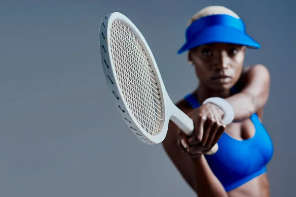 Her aim is on point. Studio shot of a sporty young woman posing with a tennis racket against a grey background. — Photo