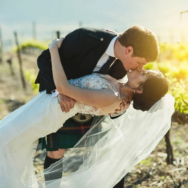 Que beijo deslumbrante. Tiro de uma noiva alegre e noivo compartilhando um beijo juntos fora ao lado de vinhas durante o dia. — Fotografia de Stock