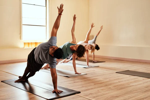 Lighten up your life with yoga. Shot of a group of young men and women practicing yoga in a fitness class. — ストック写真