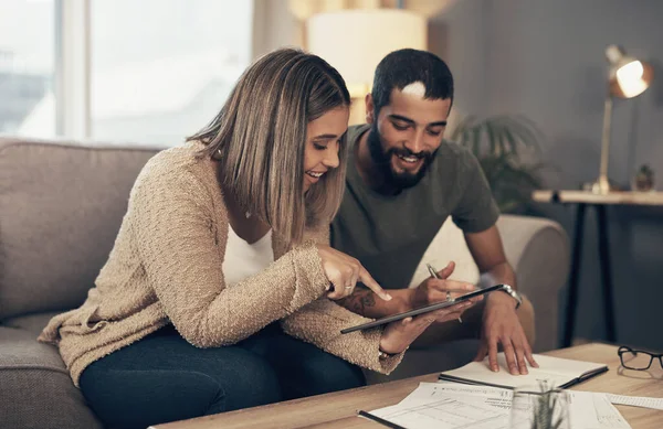 Melhorando suas finanças um toque de cada vez. Tiros de um jovem casal cantam um tablet digital enquanto passam pela papelada em casa. — Fotografia de Stock