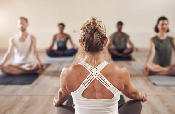 Yoga traz equilíbrio para nossas vidas. Rearview tiro de um instrutor de ioga instruindo sua classe em estúdio. — Fotografia de Stock