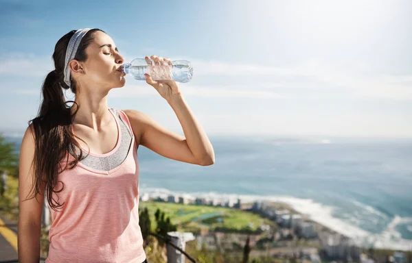 Filling up after a good run. Cropped shot of a young woman drinking a bottle of water while out exercising. — Stock Photo, Image