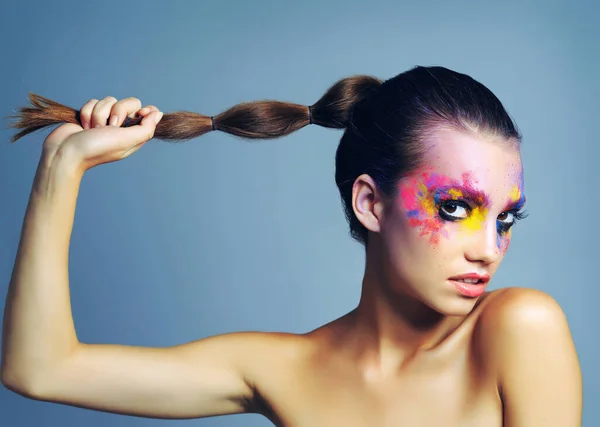 Οι βασίλισσες πολεμίστριες φοράνε μακιγιάζ σαν μπογιές. Στιγμιότυπο στούντιο μιας ελκυστικής νεαρής γυναίκας με έντονα χρωματισμένο μακιγιάζ σε μπλε φόντο. — Φωτογραφία Αρχείου