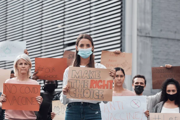 Defender os direitos humanos. Retrato recortado de uma jovem atraente segurando um sinal protestando contra a vacina covid 19 com outros manifestantes em segundo plano. — Fotografia de Stock