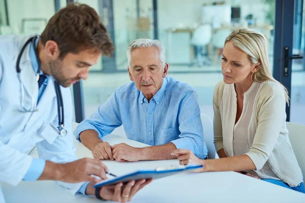 Werfen wir einen genaueren Blick auf Ihre Testergebnisse. Aufnahme eines Arztes, der mit einem älteren Patienten und seiner Tochter in einer Klinik über Papierkram diskutiert. — Stockfoto