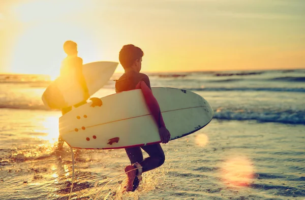 落ち着いてサーフィンを続けてください。海に入りながらサーフボードを背負った二人の弟のショット. — ストック写真