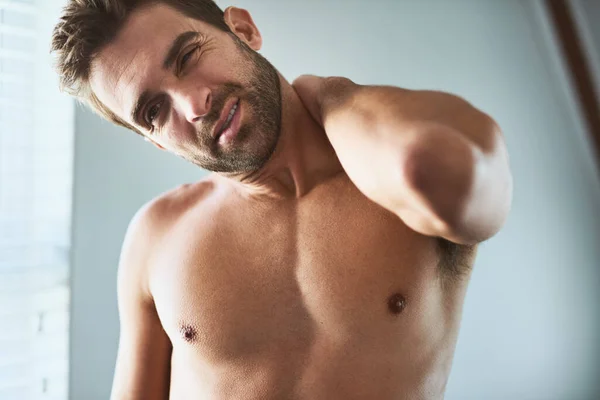 I must have slept weirdly last night. Shot of an uncomfortable looking shirtless young man holding his neck in discomfort due to pain inside at home. — Foto de Stock