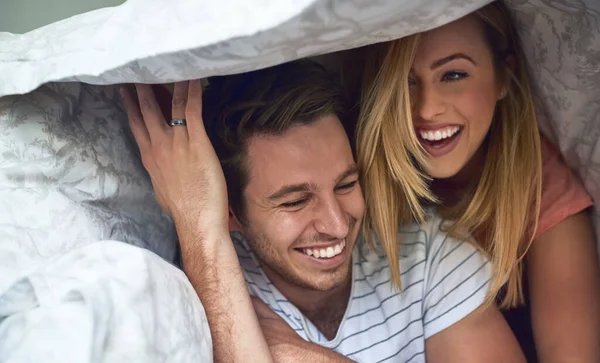 Aventuras bajo el edredón. Foto de una feliz pareja joven divirtiéndose bajo un edredón en la cama. —  Fotos de Stock