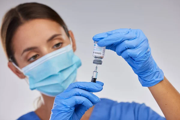 ワクチンをできるだけ普及させることが重要である。スタジオを背景に注射器にワクチン液を充填する看護師のショット. — ストック写真