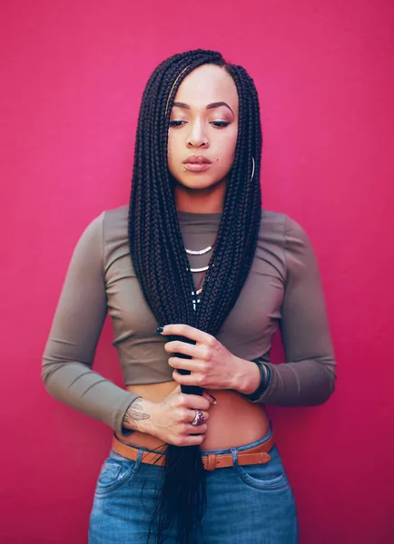Be true to who you are. Shot of an attractive young woman with braids posing against a pink background. — Photo