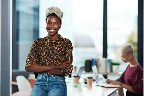 We stay creative and reap the results. Cropped portrait of an attractive young businesswoman sitting on the desk in her office while her colleague works behind her. — Stock Photo, Image