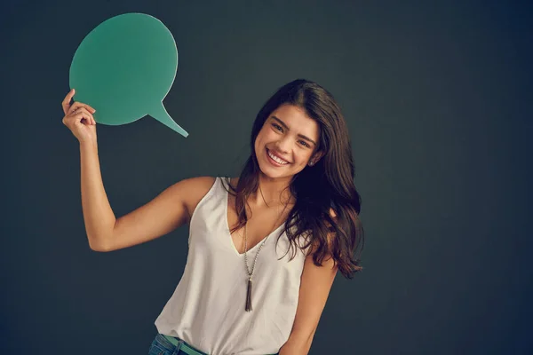 Estou a falar a sério. Estúdio tiro de uma jovem alegre segurando uma bolha de discurso enquanto está em pé contra um fundo escuro. — Fotografia de Stock