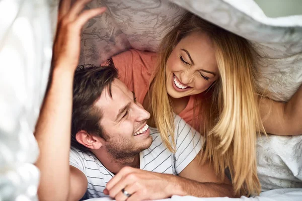 Guck mal, ich sehe dich. Aufnahme eines glücklichen jungen Paares, das Spaß unter einer Bettdecke im Bett hat. — Stockfoto