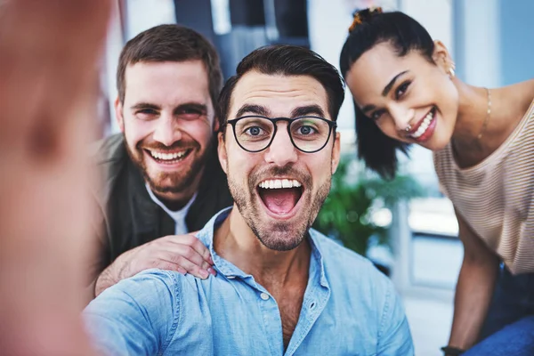 Son un equipo alegre y optimista. Fotografía de un grupo de diseñadores tomando selfies juntos en una oficina. —  Fotos de Stock