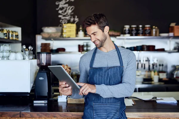 Gestionar su sitio web de negocios. Recortado disparo de un guapo joven camarero usando una tableta en su cafetería. — Foto de Stock