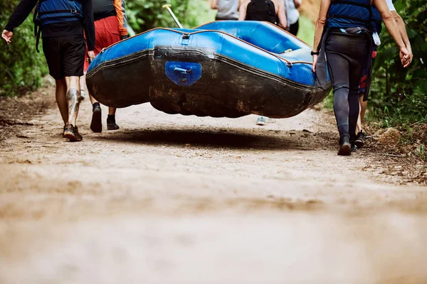 Almost there guys. Low angle shot of a group of unrecognizable people carrying a rubber boat together to go river rafting outside during the day. — 스톡 사진